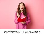 Excited young woman have excellent idea, writing down her ideas in planner, holding notebook diary and smiling amazed, standing over pink background