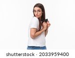 Small photo of Portrait of greedy and funny young woman unwilling to give her credit card, hiding it and looking with disbelief and reluctance, have money but dont like share, standing white background