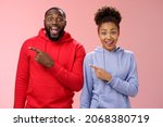 Small photo of Impressed two best friends african american man woman 25s drop jaw amused visit awesome interesting park pointing left index fingers widen eyes thrilled having fun together, standing pink background