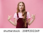 Small photo of Self-assured arrogant young female student with high ego standing cocky and brag about herself pointing at her with cool snobbish look looking away to right with contempt posing over pink wall