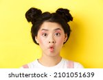 Small photo of Close-up of teen korean girl pucker lips and looking funny at camera, standing with glamour makeup and stylish hairstyle, yellow background