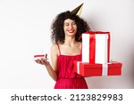 Happy birthday girl in red dress, celebrating and holding gifts with bday cake, standing on white background