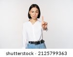 No. Young serious and confident asian woman showing stop, one finger gesture, taboo sign, standing over white background