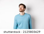 Small photo of Image of cute and silly man waiting for kiss, pucker lips with closed eyes, standing over white background