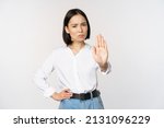 Portrait of young woman extending one hand, stop taboo sign, rejecting, declining something, standing over white background