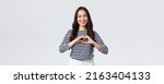 Small photo of Lifestyle, people emotions and casual concept. Lovely smiling adorable asian woman showing heart sign and smiling, express sympathy or care, standing white background