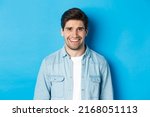 Small photo of Close-up of young man feeling awkward, smile and cringe from uncomfortable situation, standing over blue background