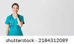 Small photo of Covid-19, healthcare workers, pandemic concept. Cheerful, smiling female asian nurse in scrubs having secret, making surprise, showing shush gesture, shhh keep quiet, standing white background