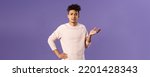 Small photo of So what, why asking. Portrait of unbothered and careless, ignorant young man dont care on people rules, raising hand in dismay and confusion, being puzzled, look uninterested, purple background
