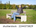 Portrait of happy asian girl feeling freedom and excitement, stretching hands while sitting on bench and smiling.