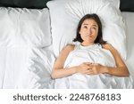 Small photo of Portrait of asian girl lying in her bed and shrugs, looks puzzled, overthinking before going to sleep, looking complicated at camera.