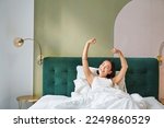 Portrait of smiling happy asian girl, wakes up feeling enthusiastic, stretches her hands up, enjoys good morning in her bedroom.