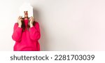 Small photo of Real estate. Funny asian middle-aged woman hiding face behind paper house model and showing puckered lips, having fun, standing over white background.