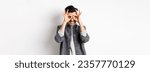 Small photo of Smiling guy looking left at logo through hand binoculars, see good dea and look satisfied, standing on white background.
