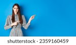 Small photo of Angry frowning woman pointing fingers right and condemn person, feeling disapointed, standing in dress on blue background.