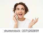 Small photo of Portrait of happy, chatty young woman talking on mobile phone, using smartphone, calling someone, standing over white studio background.