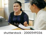 Small photo of Happy Asian blind person woman with vintage braille typewriter or Brailler for people with vision disabilities, working and talking with senior colleague woman in office workplace.