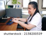 Asian woman with blindness disability using computer with refreshable braille display or braille terminal a technology assistive device for persons with visual impairment in workplace.