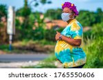 Beautiful pregnant African mother or woman wearing face mask for protection and holding abdomen-concept on obstetrics in covid-19 pandemic