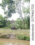 Small photo of Vehicle passing on road or sepeda motor lewat di jalan inspeksi selokan mataram, saluran irigasi pertanian yang panjang dibangun atas prakarsa Raja Jogja di yogyakarta, Indonesia, July 18, 2022