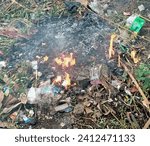 Small photo of burning out the garbage, Indonesia, January 14,2024 burning rubbish, plastic, inorganic, burnt, with fire, in an open area, the fire engulfs the rubbish, white smoke billows, the rubbish is completely