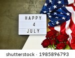 Light box with text HAPPY 4 JULY and flowers roses, USA flag on a gray and white background. Flat lay. Independence Day USA concept. Greeting card.
