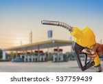 Holding a fuel nozzle against with gas station blurred background.