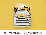 Small photo of Opened School backpack with stationery on yellow background. Concept back to school. School supplies with white school bag.