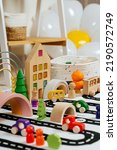 Small photo of A toy town built in a children's room. Road, cars, trees and wooden blocks for children's games in playroom. Educational game for baby and toddler in modern nursery.