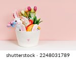 Baby Easter Basket gifts. White  Easter Basket with Easter Bunny, eggs, flowers, candy and toys on pink background. Holidays decorations.  