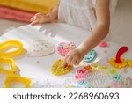 Small photo of Child hands creating Easter eggs from play dough decoration with beads. Cute children's crafts for Easter. Holiday Art Activity for Kids. Fine motor skills, creativity and hobby.