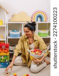 Small photo of Mom sorted by colors and puts children's toys in transparent boxes and storage baskets. Mother tidy up the childrens room. Organization and Storage Ideas in playroom.