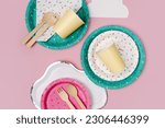 Cute paper party plates and cups for themed kids party on pink background. Birthday party decorations and props in bright colors. Set of holiday disposable tableware for party or picnic. 