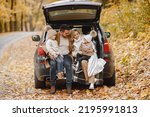 Small photo of Young family sitting at open trunk of hatchback car in autumn forest
