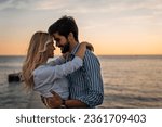 Lovely couple bonding at the beach in summer. Romantic male and female looking each other into eyes during the sunset. Beautiful couple in love standing face to face.