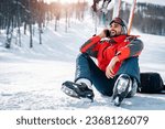 Smiling male skier sitting on snow taking a break while using smart phone and laughing. Handsome bearded guy having a fun engaging call with his friend.