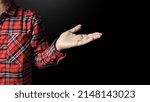 Small photo of A man in a red and black plaid shirt spreads his hands in a salutary gesture on a black background.