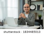 Small photo of A middle-aged man around the age of 35. Working at home Work through the laptop by meeting video conference. He was wearing a grey suit and glasses. Smiling asian businessman work from home.