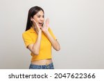 Small photo of Excited asian woman shout out loud wow with hands on isolated background. Happy shocked face female wow promotion advertising concept. Joyful teenage girl in yellow shirt standing in white room.