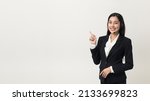 Small photo of Happy young asian business woman call centre pointing finger to blank space. Welcome female operator put on smalltalk headphone standing on isolated white background.