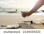 Small photo of Close up woman hand pick up the plastic bottle on the beach. Female Volunteer clean the trash on the beach make the sea beautiful. World environment day concept.