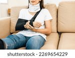 Small photo of Happy woman recovery from accident fracture broken bone injury with leg splints in cast neck splints collar arm splints sling support arm in living room. Social security and health insurance concept.