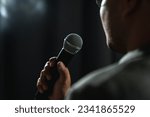 Small photo of Confident successful speaker man talking on stage with spotlight strike through the darkness at corporate business event. Public speaker giving talk at conference hall. Stand up comedian.