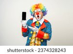 Small photo of Mr Clown. Portrait of Funny face Clown man in colorful uniform standing holding smartphone. Happy expression male bozo in various pose with cellphone on isolated background.