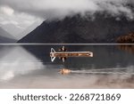 duck swimming calmly in the calm water of the lake while a big bird moves its wings standing on the wooden platform between the big mountains under a threatening sky of clouds and storm, Nelson lakes
