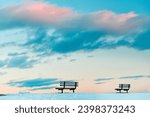 Two benches on a snow-covered glade against the backdrop of a gentle sunset sky. Minimalism.
