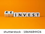 Reinvest symbol. Inverted wooden cubes with words 'invest - reinvest'. Beautiful orange background. Business and reinvest concept. Copy space.