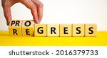 Small photo of Regress or progress symbol. Businessman turns wooden cubes and changes the word 'regress' to 'progress'. Beautiful yellow table, white background, copy space. Business, regress or progress concept.