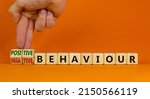 Small photo of Positive or negative behaviour symbol. Businessman turns cubes, changes words negative behaviour to positive behaviour. Orange background, copy space. Business, positive or negative behaviour concept.