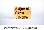 Small photo of AGI adjusted gross income symbol. Concept words AGI adjusted gross income on wooden blocks. Beautiful white background, copy space. Business and AGI adjusted gross income concept.